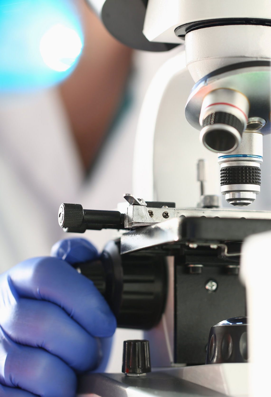 Gloved analyst adjusting a laboratory microscope